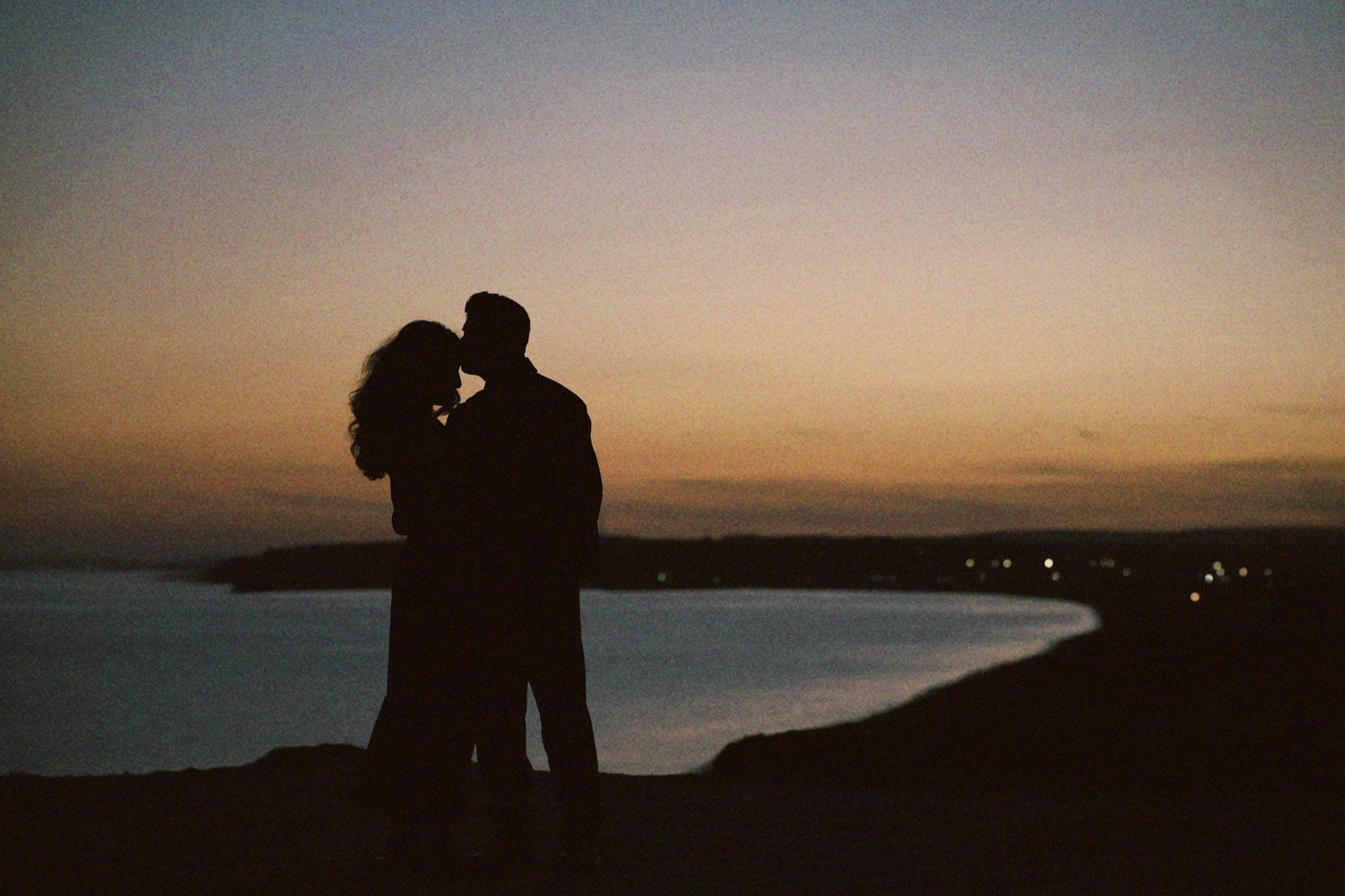 Arun and Anaina silhouetted against the sunset, sharing a kiss over the sea